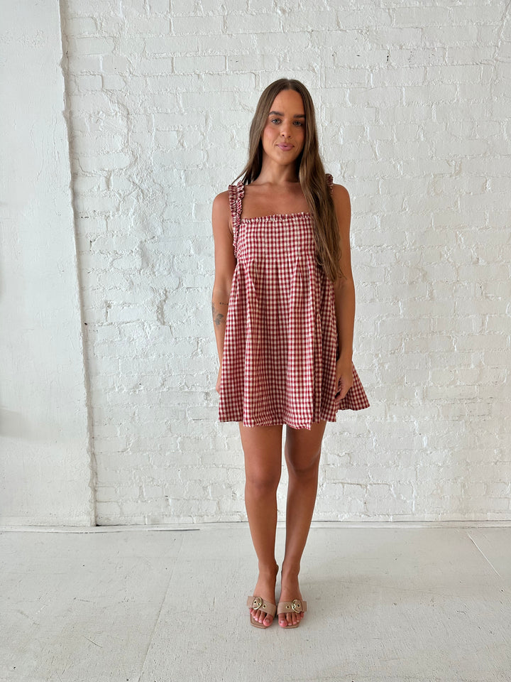 Woman wearing red and beige plaid babydoll style mini dress with gathered neckline, and gathered straps.