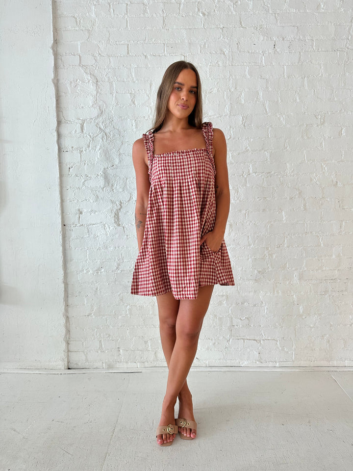 Woman wearing red and beige plaid babydoll style mini dress with gathered neckline, and gathered straps.
