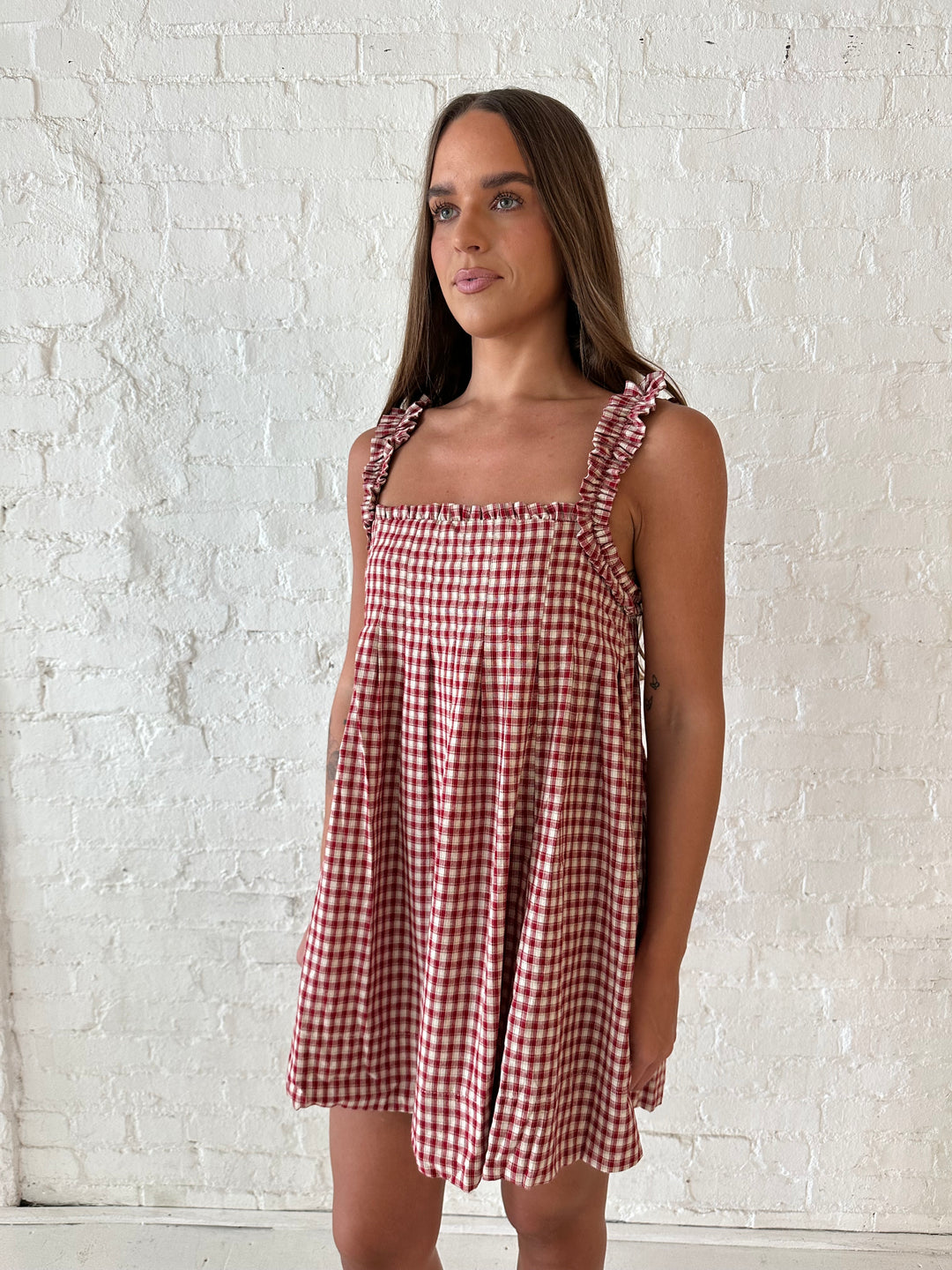Woman wearing red and beige plaid babydoll style mini dress with gathered neckline, and gathered straps.