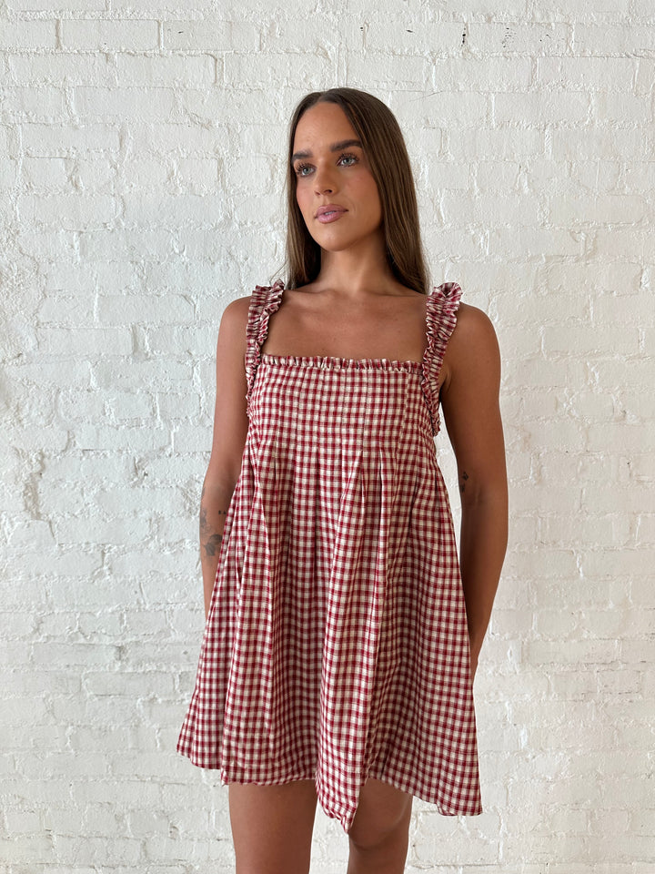 Woman wearing red and beige plaid babydoll style mini dress with gathered neckline, and gathered straps.