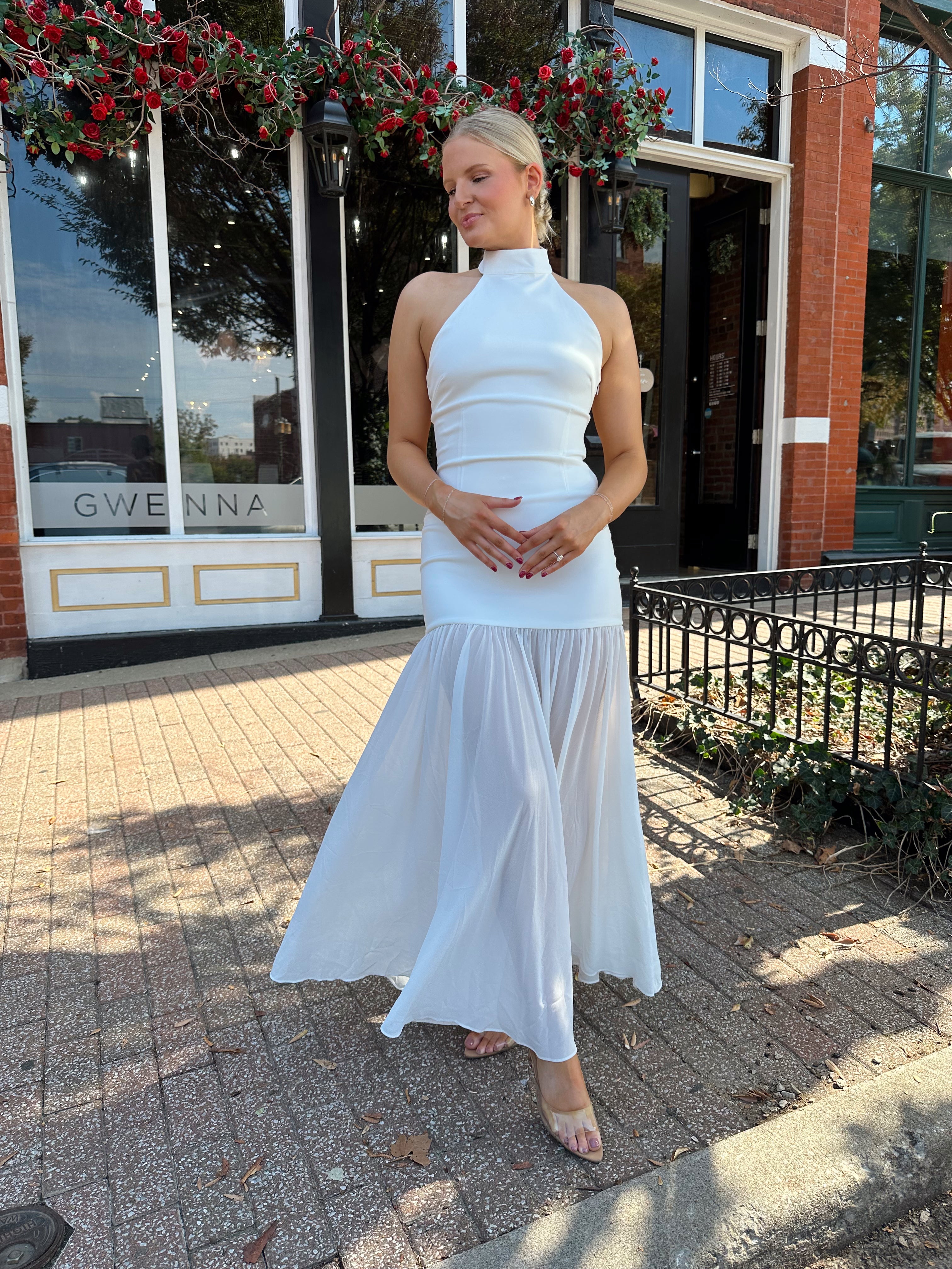 Woman wearing white halter neckline and sheer skirt overlay and open back. 