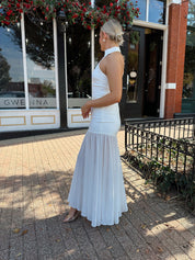 Woman wearing white halter neckline and sheer skirt overlay and open back. 