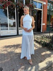 Woman wearing white halter neckline and sheer skirt overlay and open back. 