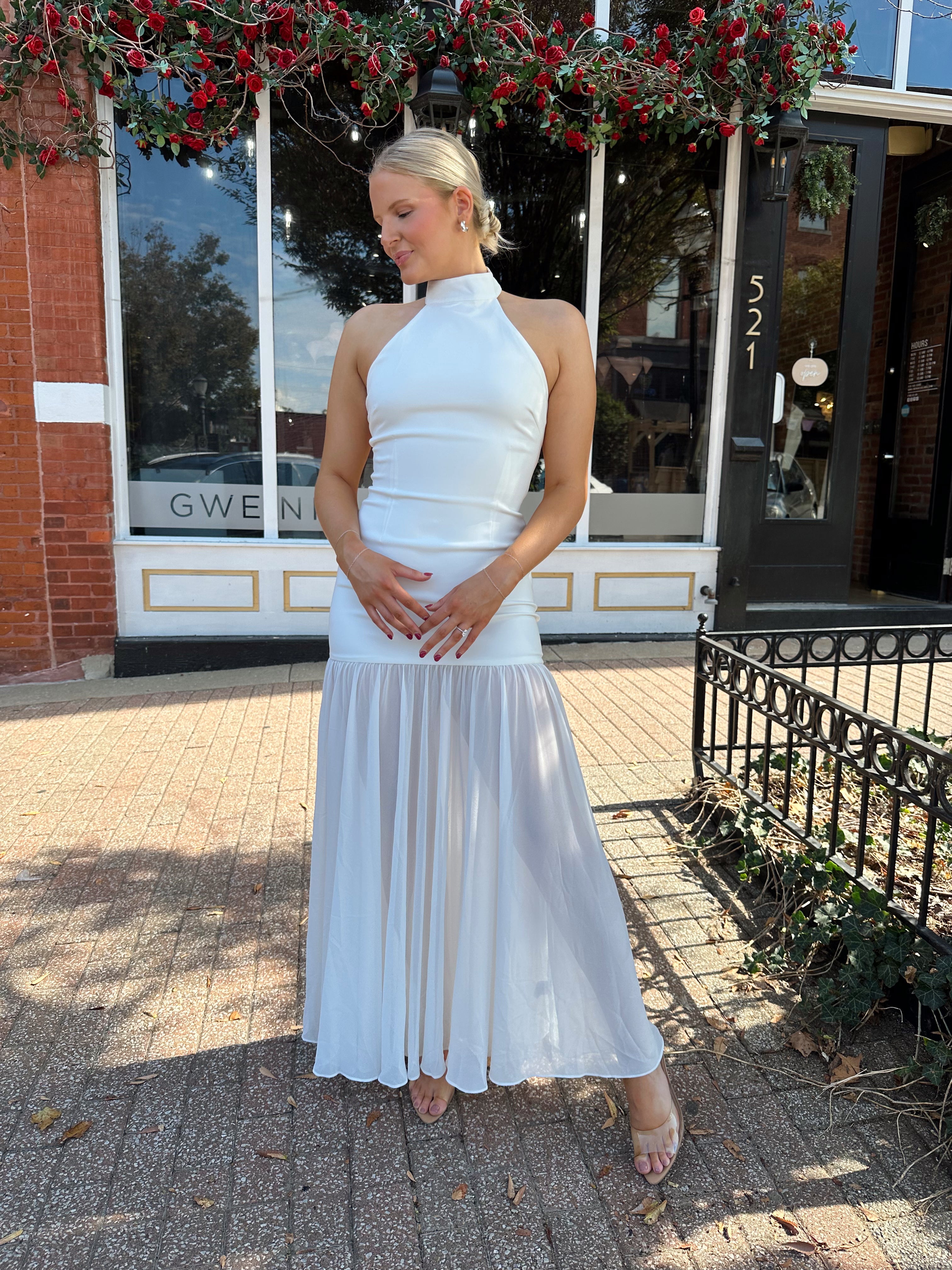 Woman wearing white halter neckline and sheer skirt overlay and open back. 