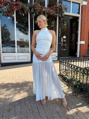 Woman wearing white halter neckline and sheer skirt overlay and open back. 