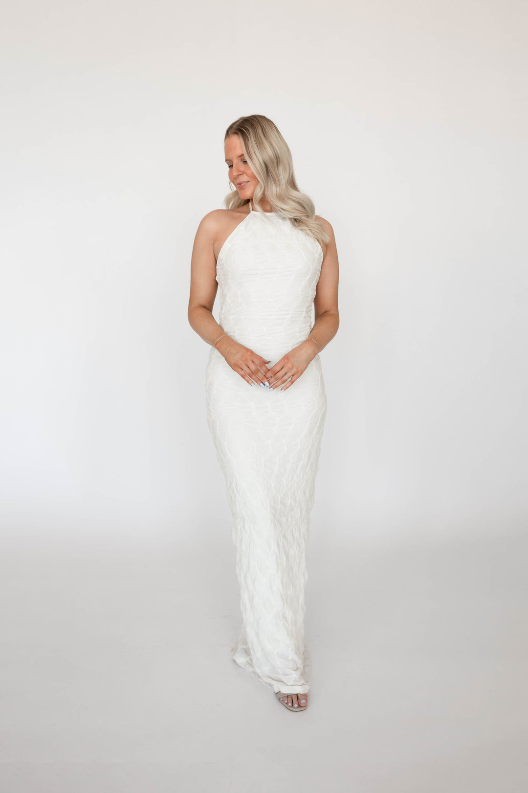 Woman wearing textured ivory knit maxi dress with open back. 