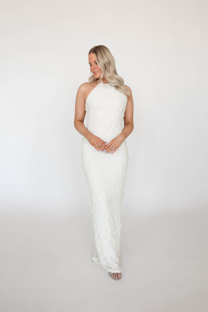 Woman wearing textured ivory knit maxi dress with open back. 