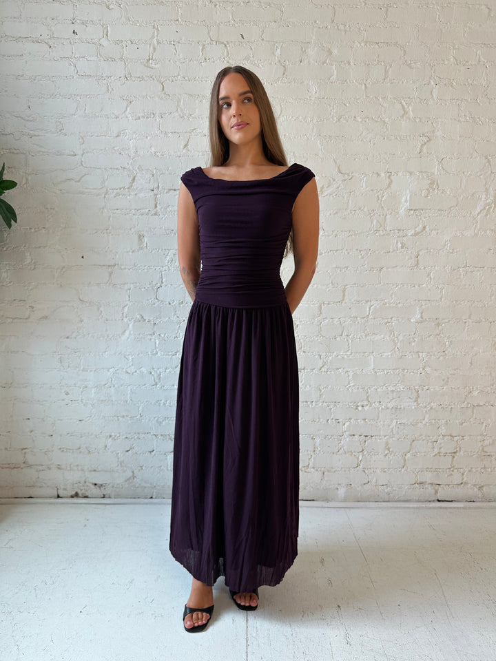 Woman wearing plum colored ruched midi dress with flowy skirt and heels.