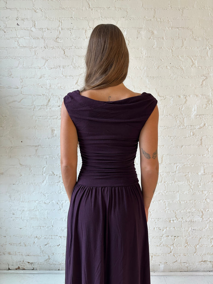 Woman wearing plum colored ruched midi dress with flowy skirt and heels.