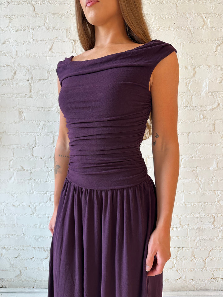 Woman wearing plum colored ruched midi dress with flowy skirt and heels.