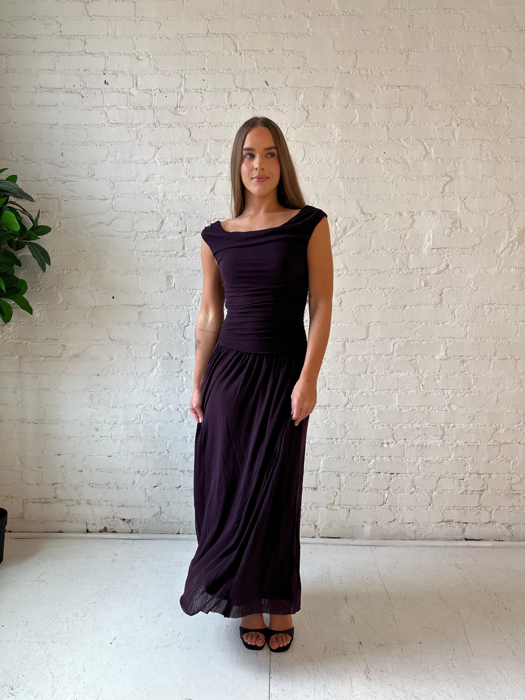 Woman wearing plum colored ruched midi dress with flowy skirt and heels.