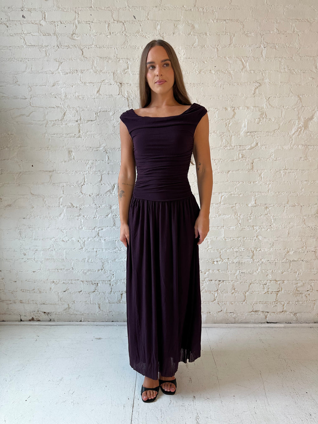 Woman wearing plum colored ruched midi dress with flowy skirt and heels.