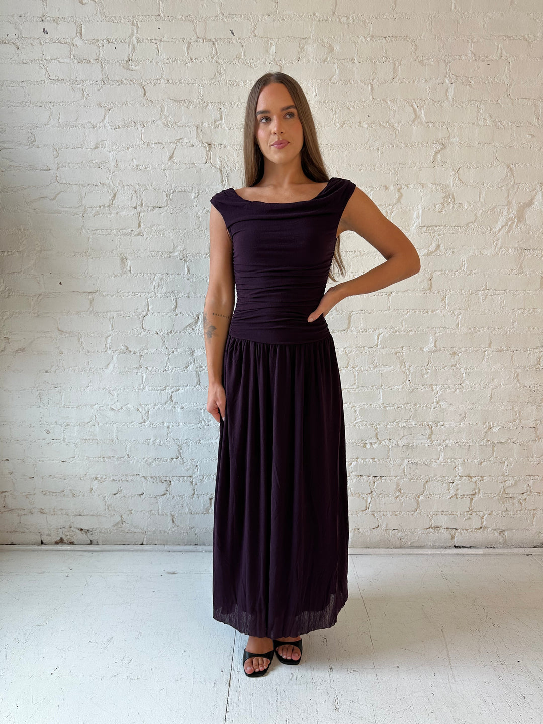 Woman wearing plum colored ruched midi dress with flowy skirt and heels.