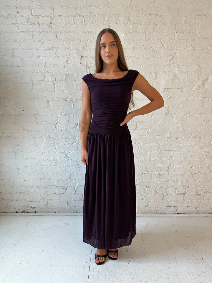 Woman wearing plum colored ruched midi dress with flowy skirt and heels.