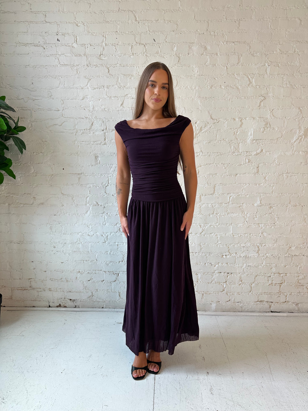Woman wearing plum colored ruched midi dress with flowy skirt and heels.
