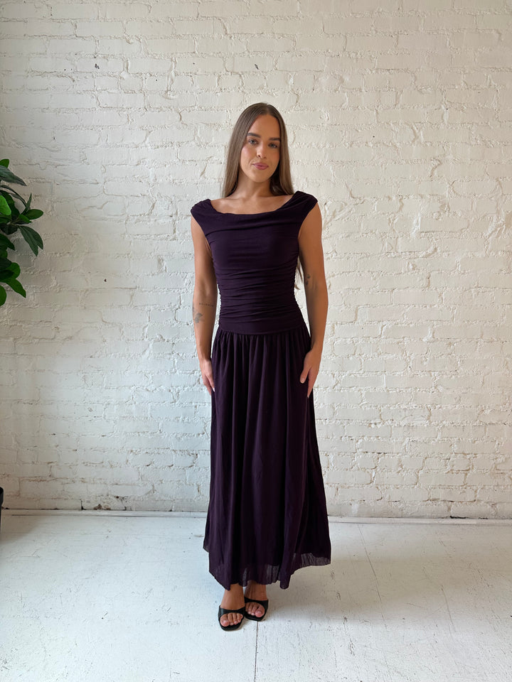 Woman wearing plum colored ruched midi dress with flowy skirt and heels.
