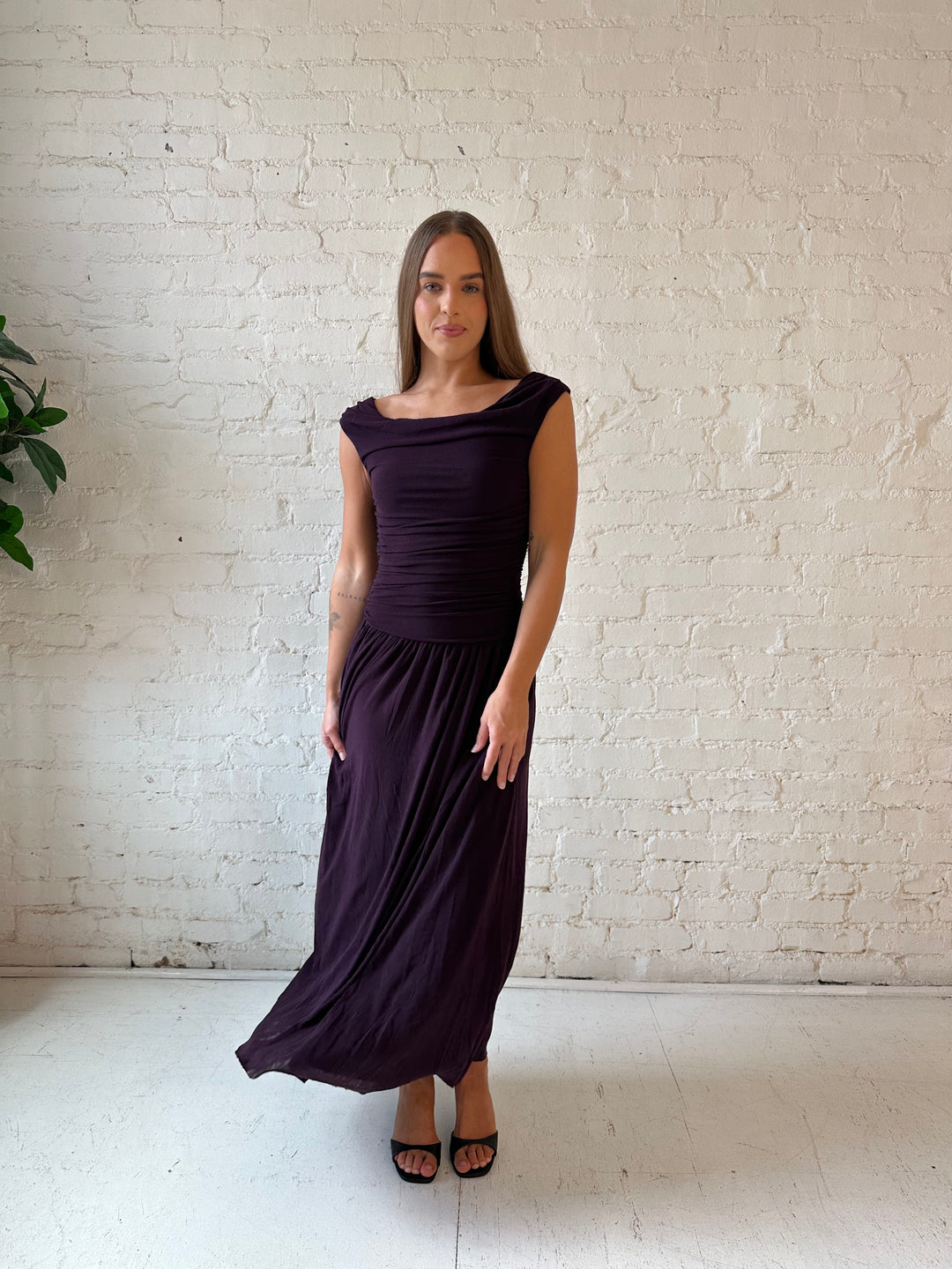 Woman wearing plum colored ruched midi dress with flowy skirt and heels.