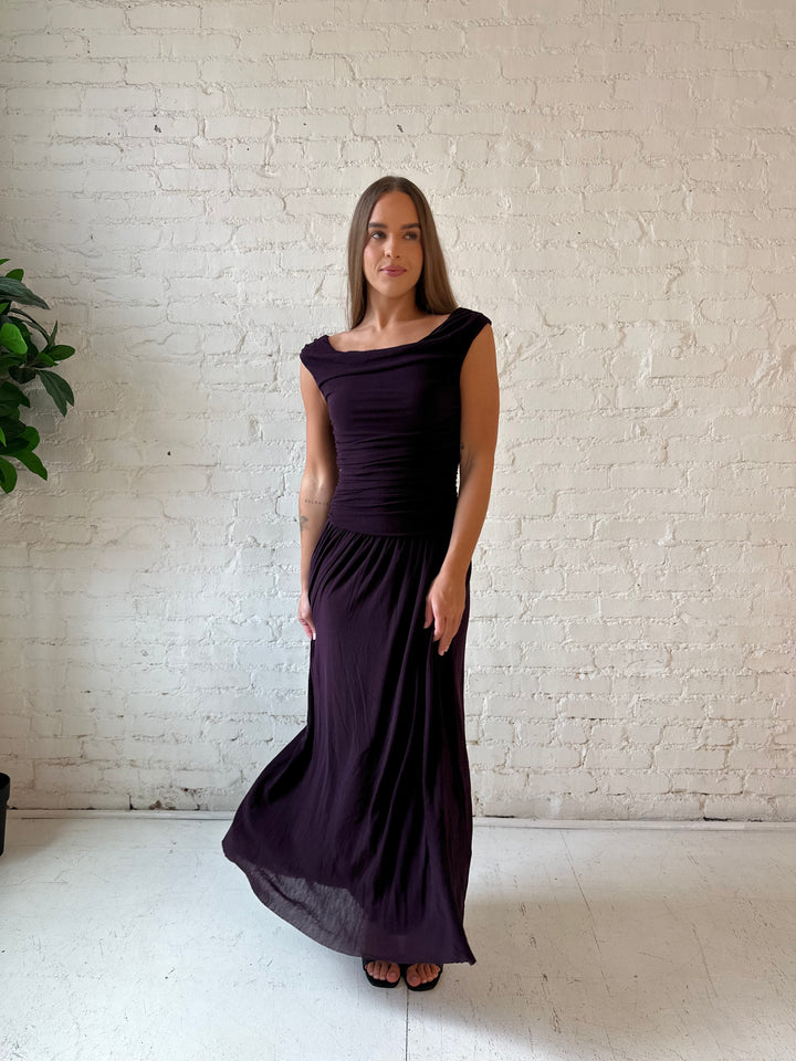 Woman wearing plum colored ruched midi dress with flowy skirt and heels.
