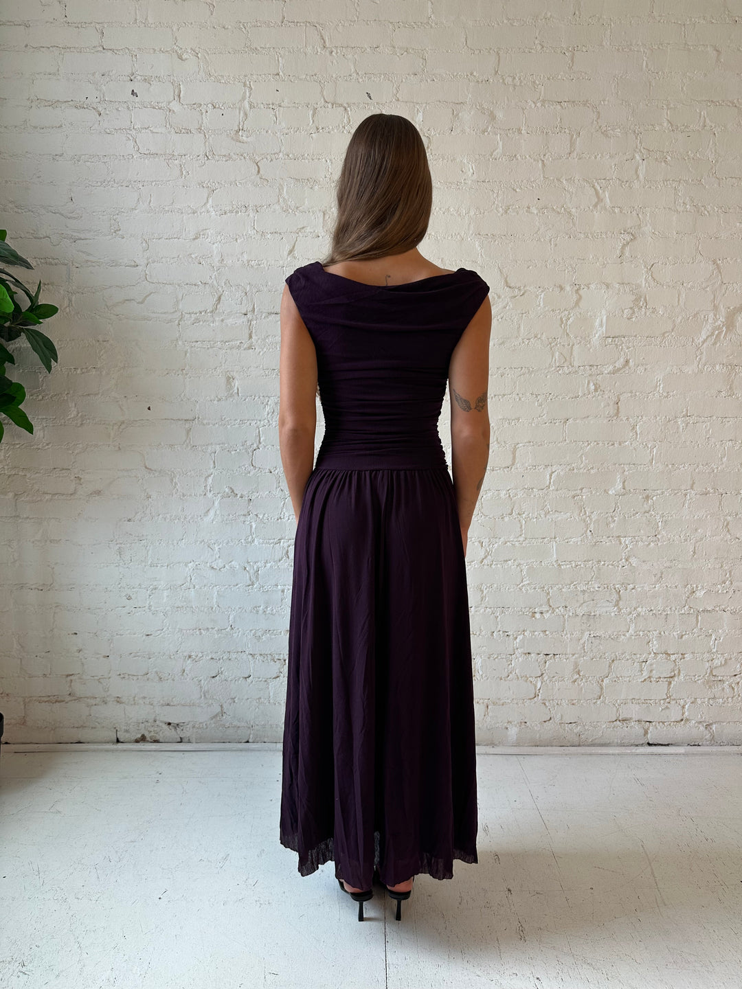 Woman wearing plum colored ruched midi dress with flowy skirt and heels.