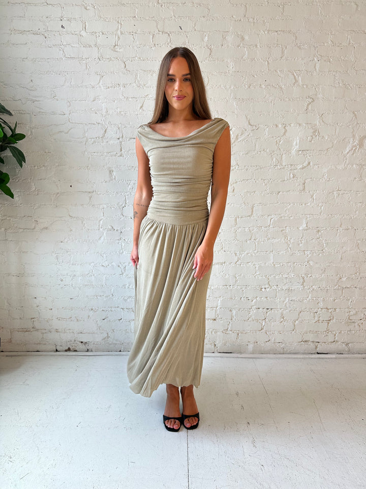 Woman wearing taupe midi dress with ruched sides and cowl neckline. 