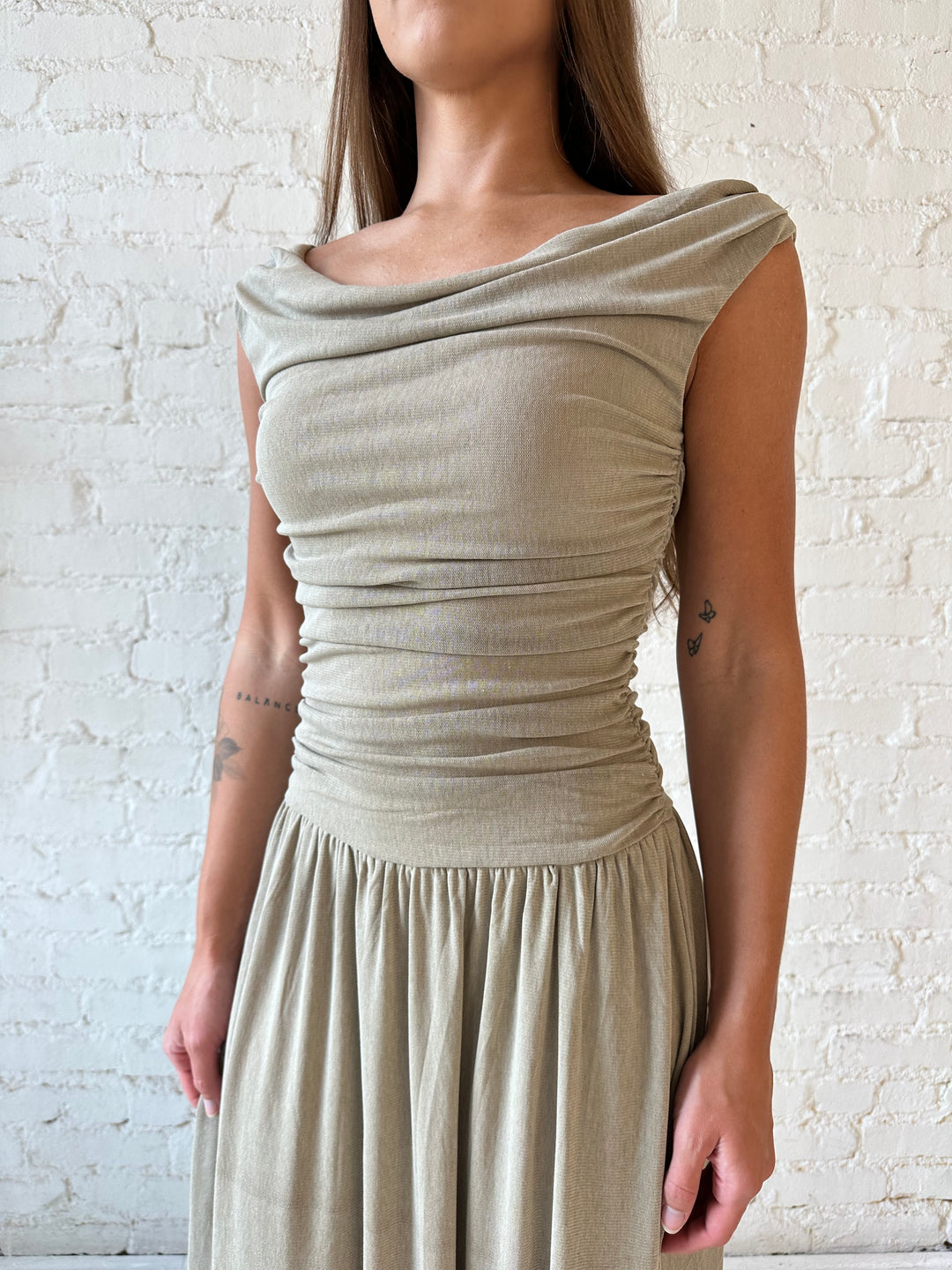 Woman wearing taupe midi dress with ruched sides and cowl neckline. 