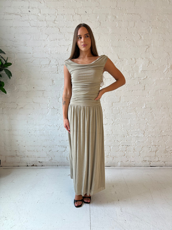 Woman wearing taupe midi dress with ruched sides and cowl neckline. 