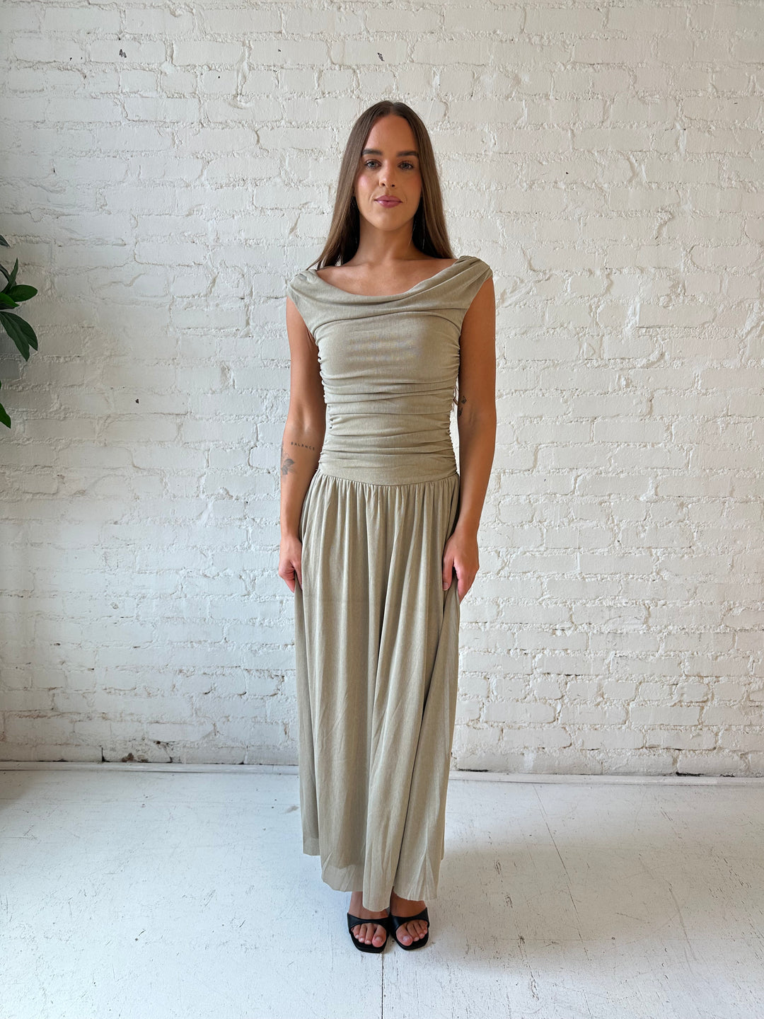 Woman wearing taupe midi dress with ruched sides and cowl neckline. 