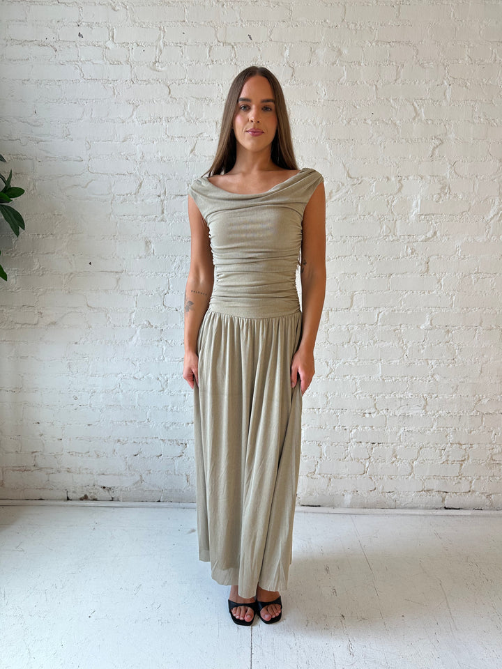 Woman wearing taupe midi dress with ruched sides and cowl neckline. 
