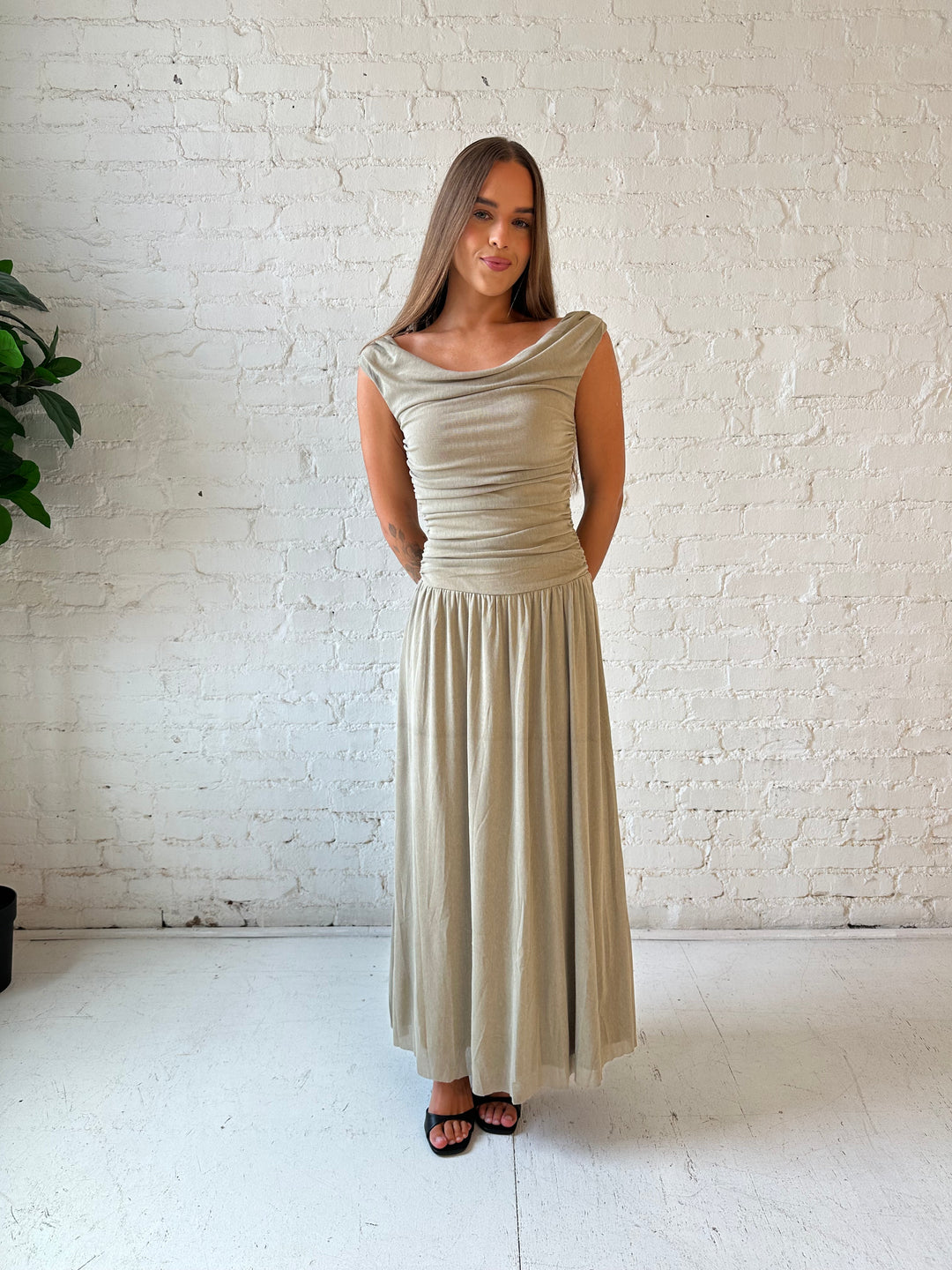 Woman wearing taupe midi dress with ruched sides and cowl neckline. 