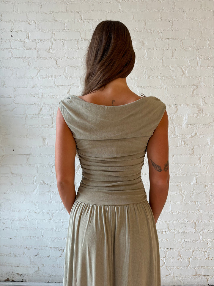 Woman wearing taupe midi dress with ruched sides and cowl neckline. 