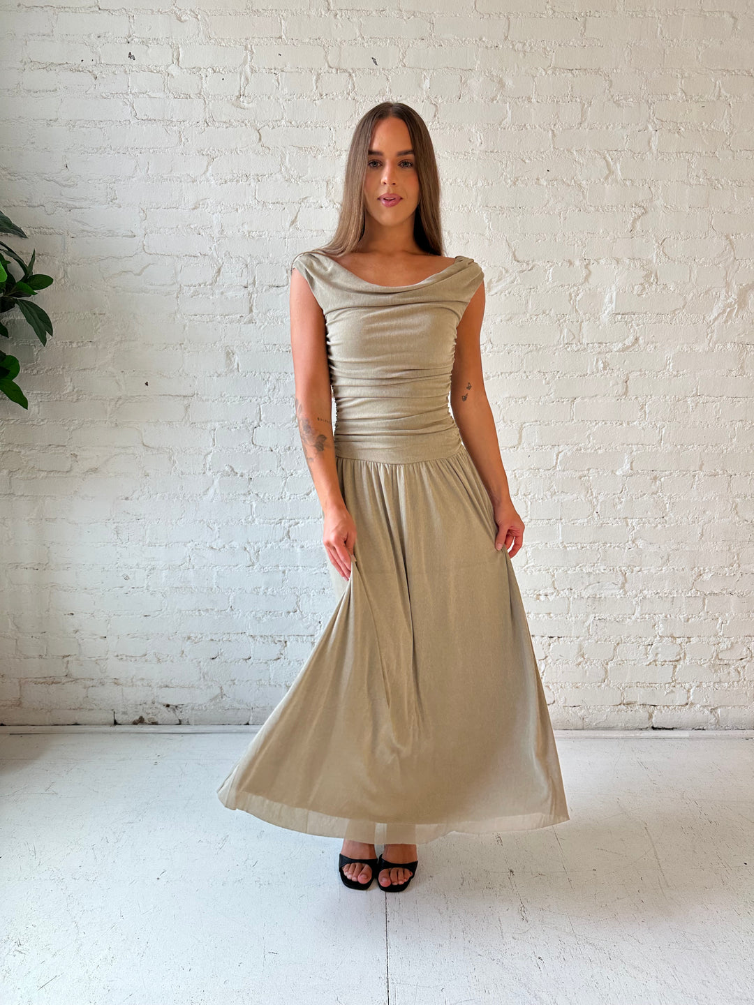 Woman wearing taupe midi dress with ruched sides and cowl neckline. 