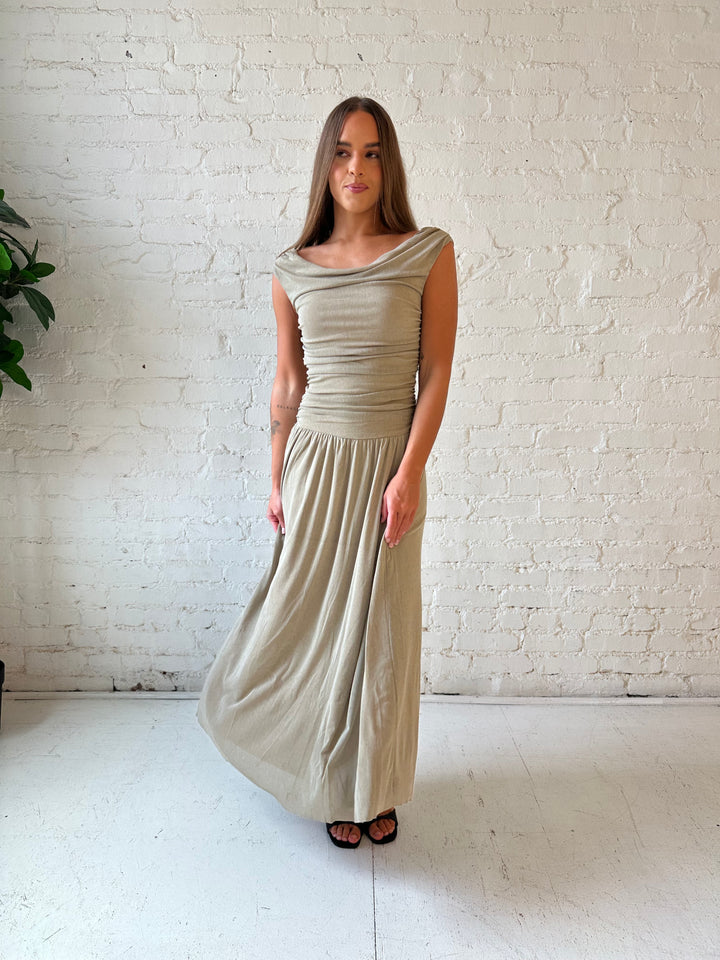 Woman wearing taupe midi dress with ruched sides and cowl neckline. 