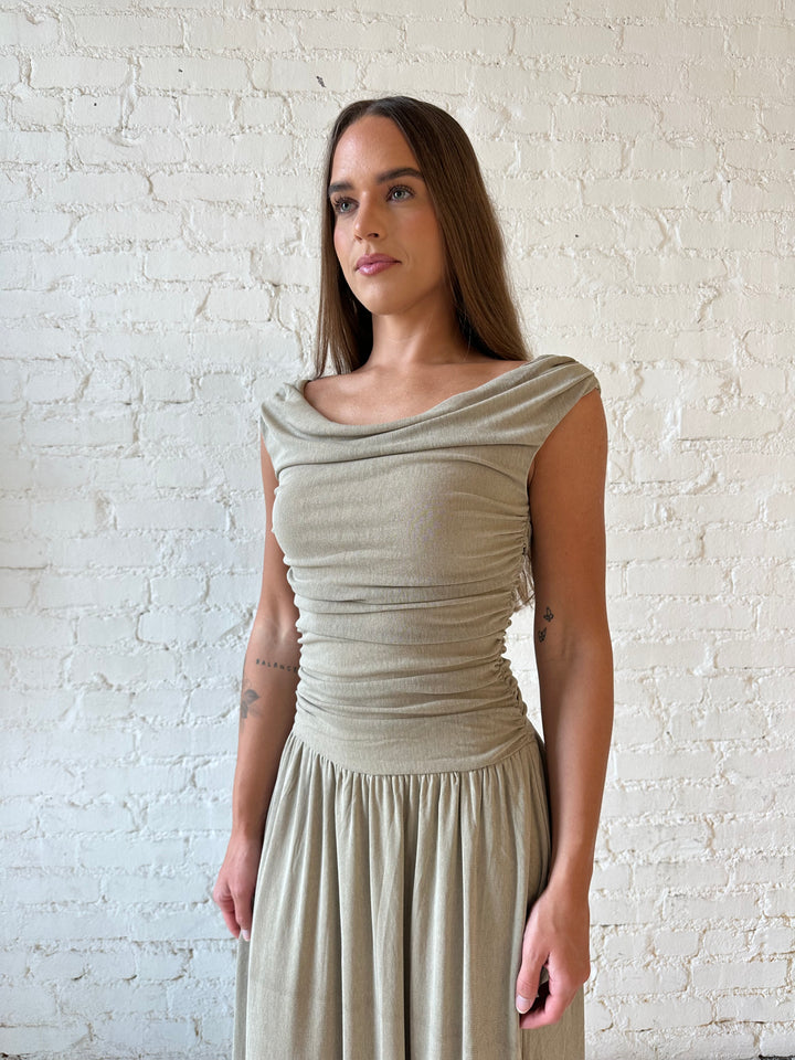 Woman wearing taupe midi dress with ruched sides and cowl neckline. 