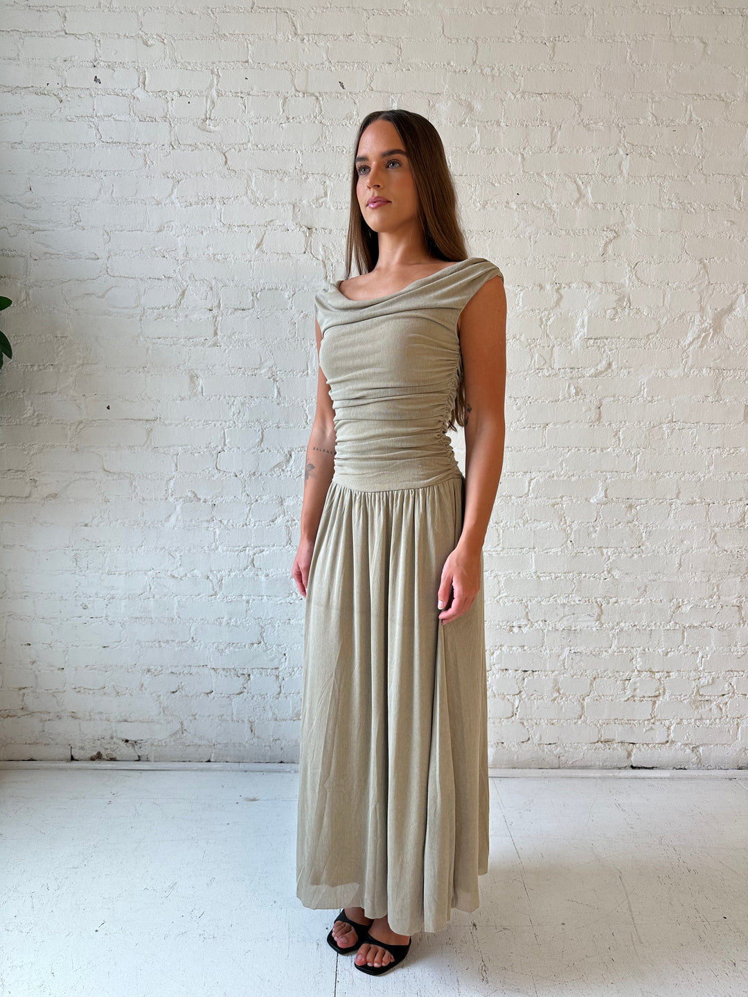 Woman wearing taupe midi dress with ruched sides and cowl neckline. 