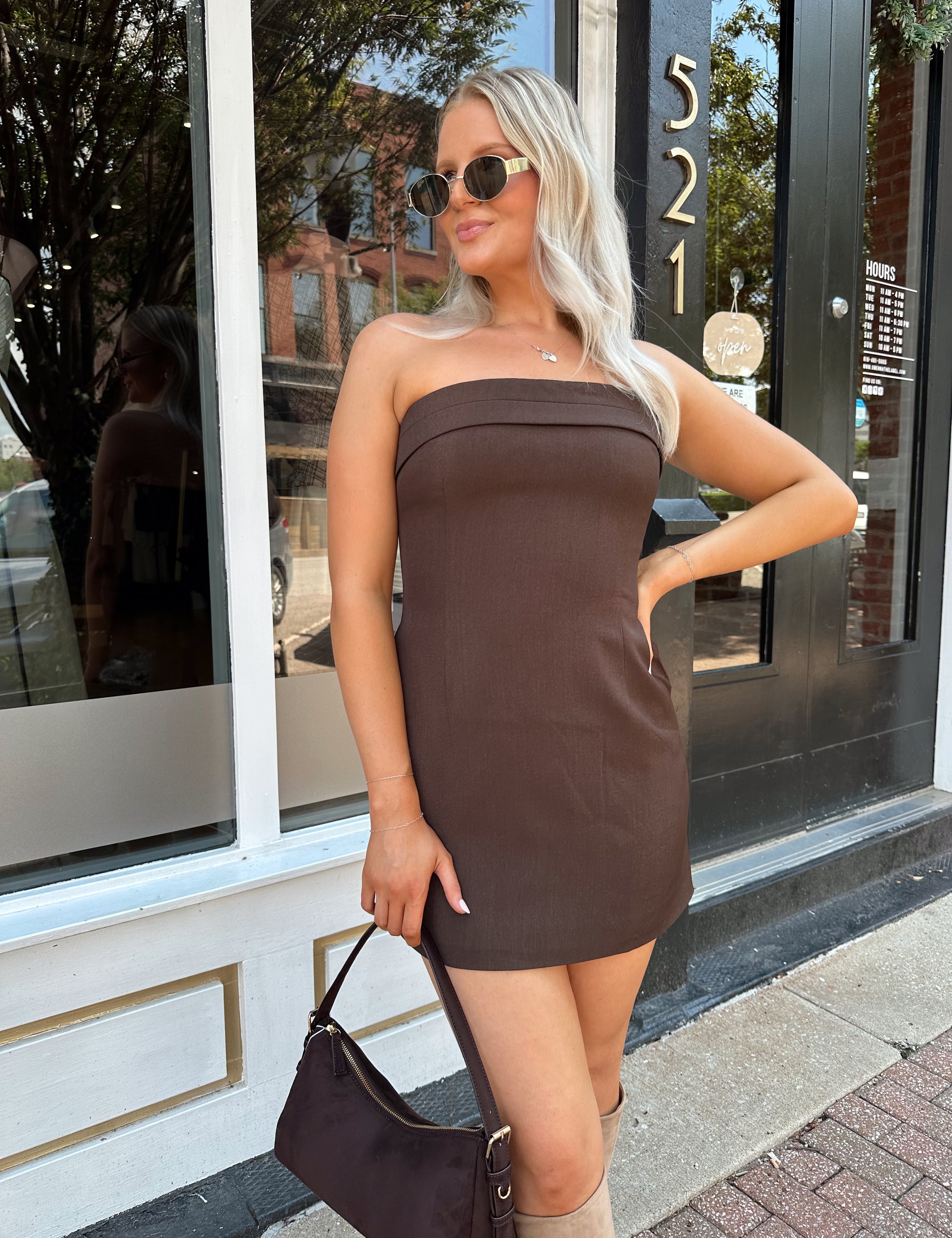 Woman wearing a dark brown strapless tailored mini dress with tan knee-high boots.