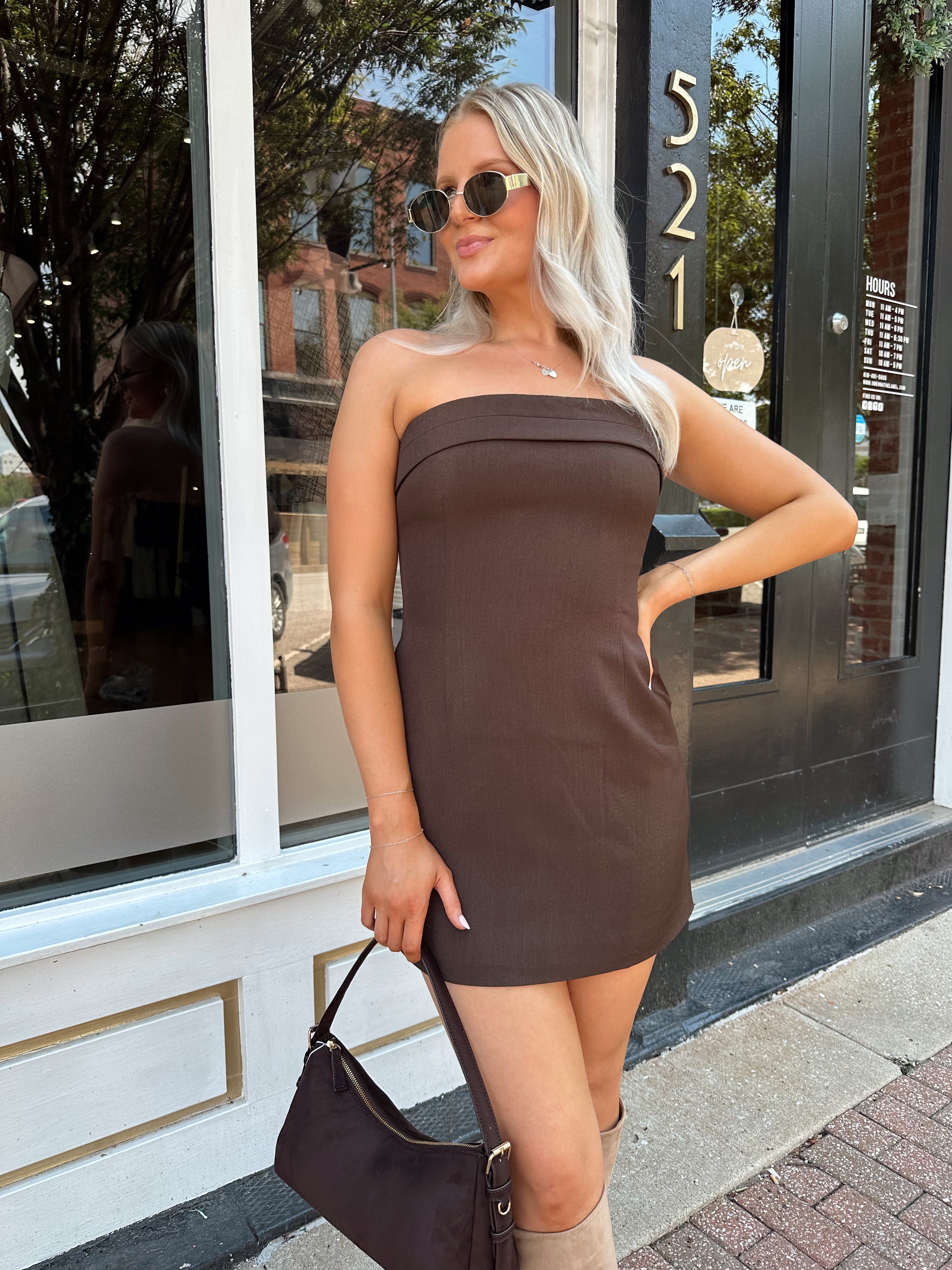 Woman wearing a dark brown strapless tailored mini dress with tan knee-high boots.