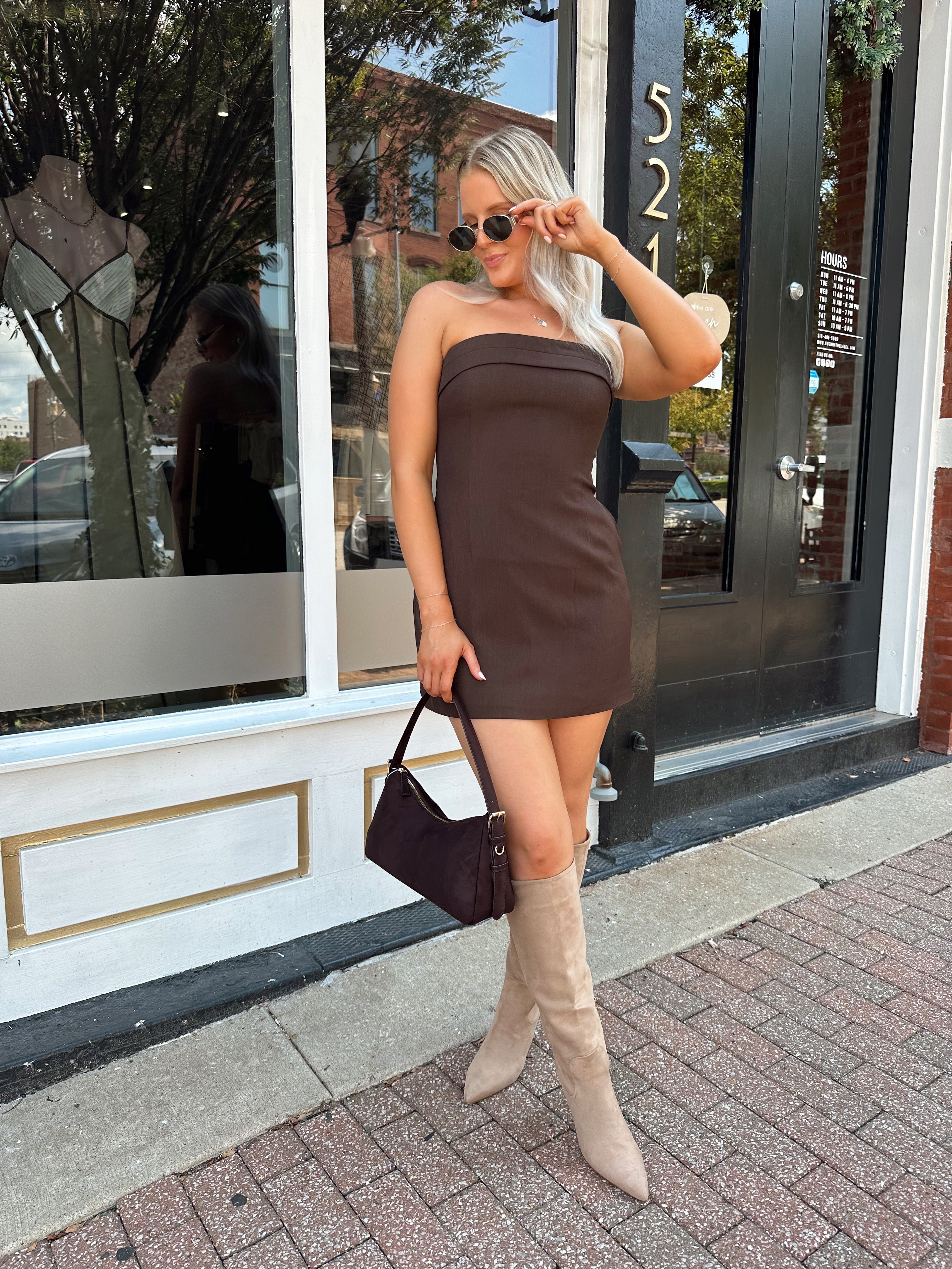 Woman wearing a dark brown strapless tailored mini dress with tan knee-high boots.