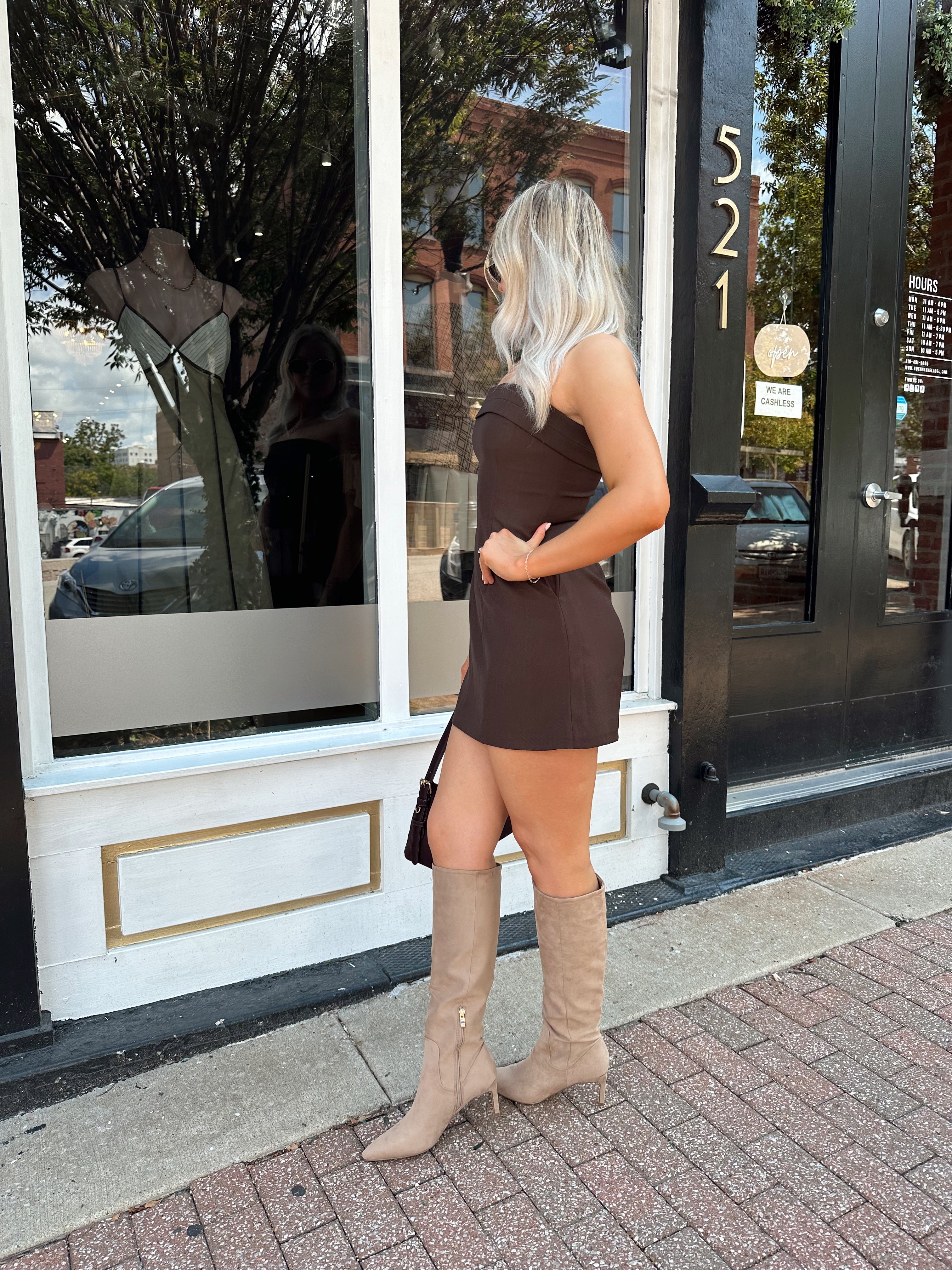 Woman wearing a dark brown strapless tailored mini dress with tan knee-high boots.