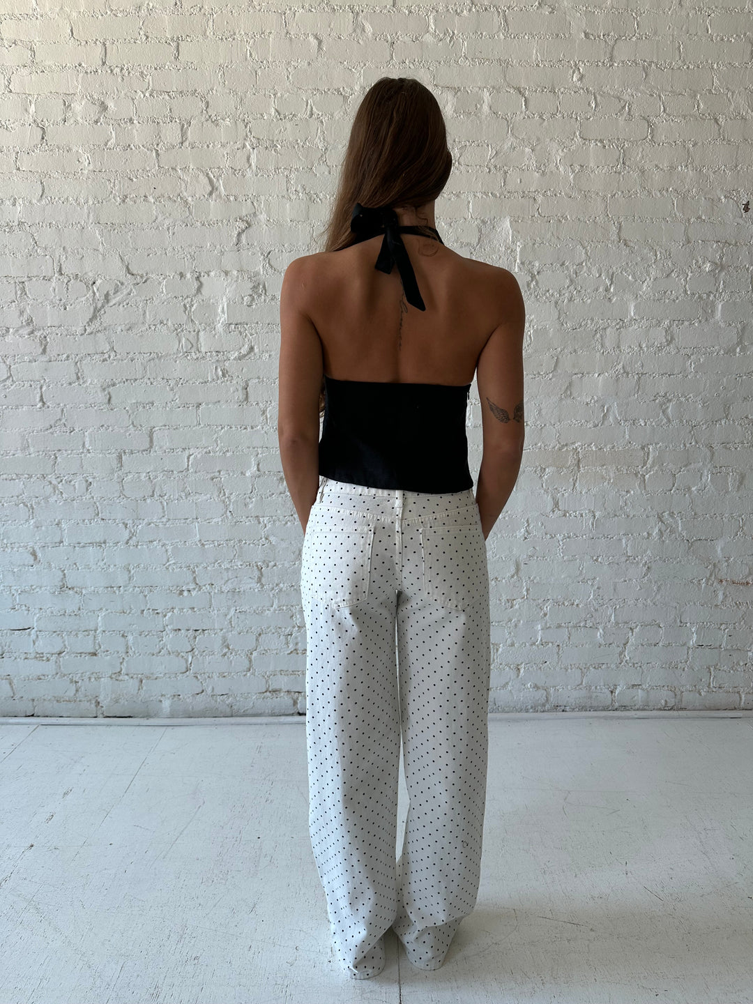 Woman wearing white and black polka dot jeans with black halter top.