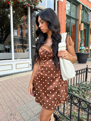 Woman wearing copper brown satin mini dress with white polka dots and self tie straps.