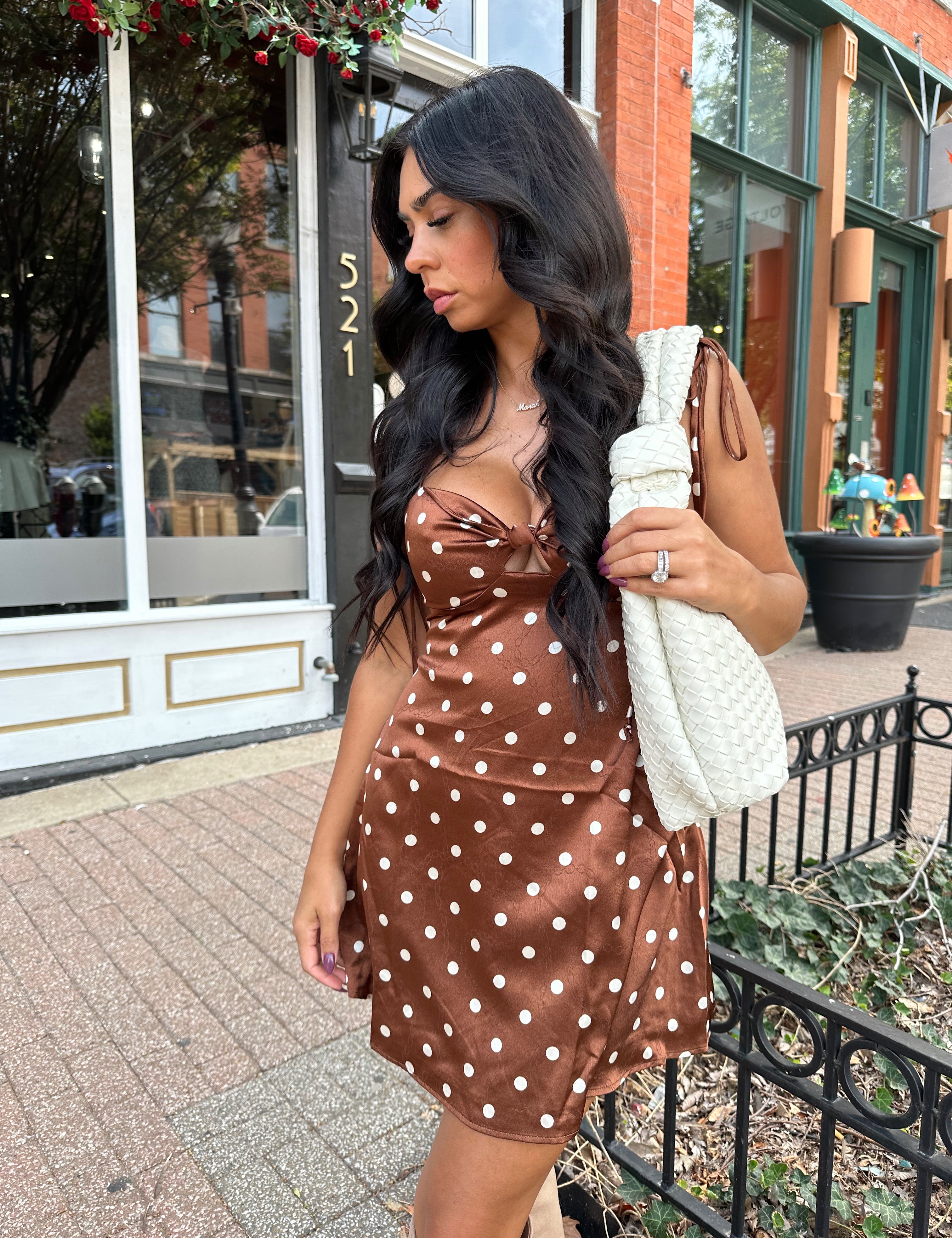 Woman wearing copper brown satin mini dress with white polka dots and self tie straps.
