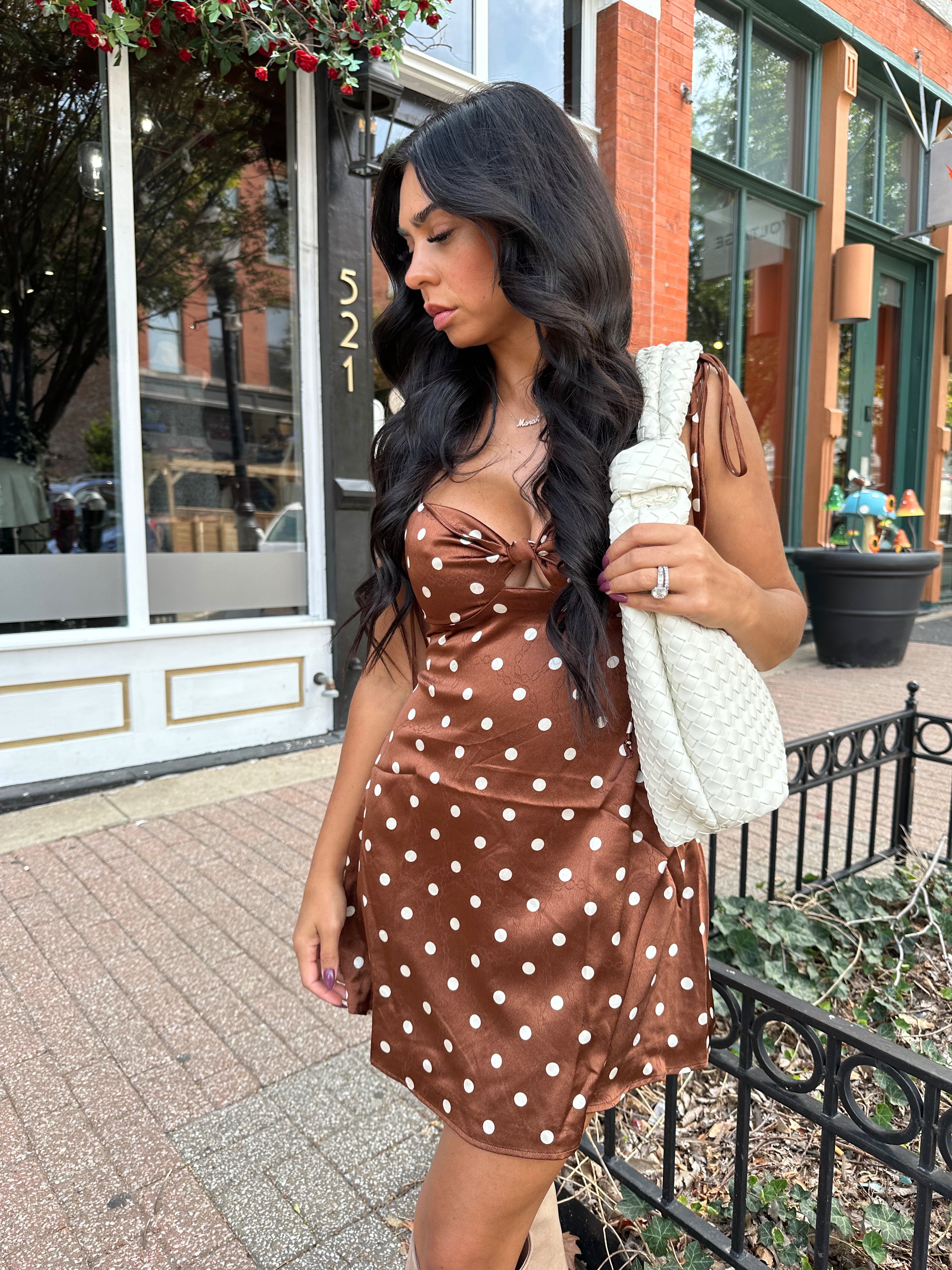 Woman wearing copper brown satin mini dress with white polka dots and self tie straps.