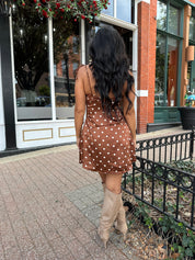 Woman wearing copper brown satin mini dress with white polka dots and self tie straps.