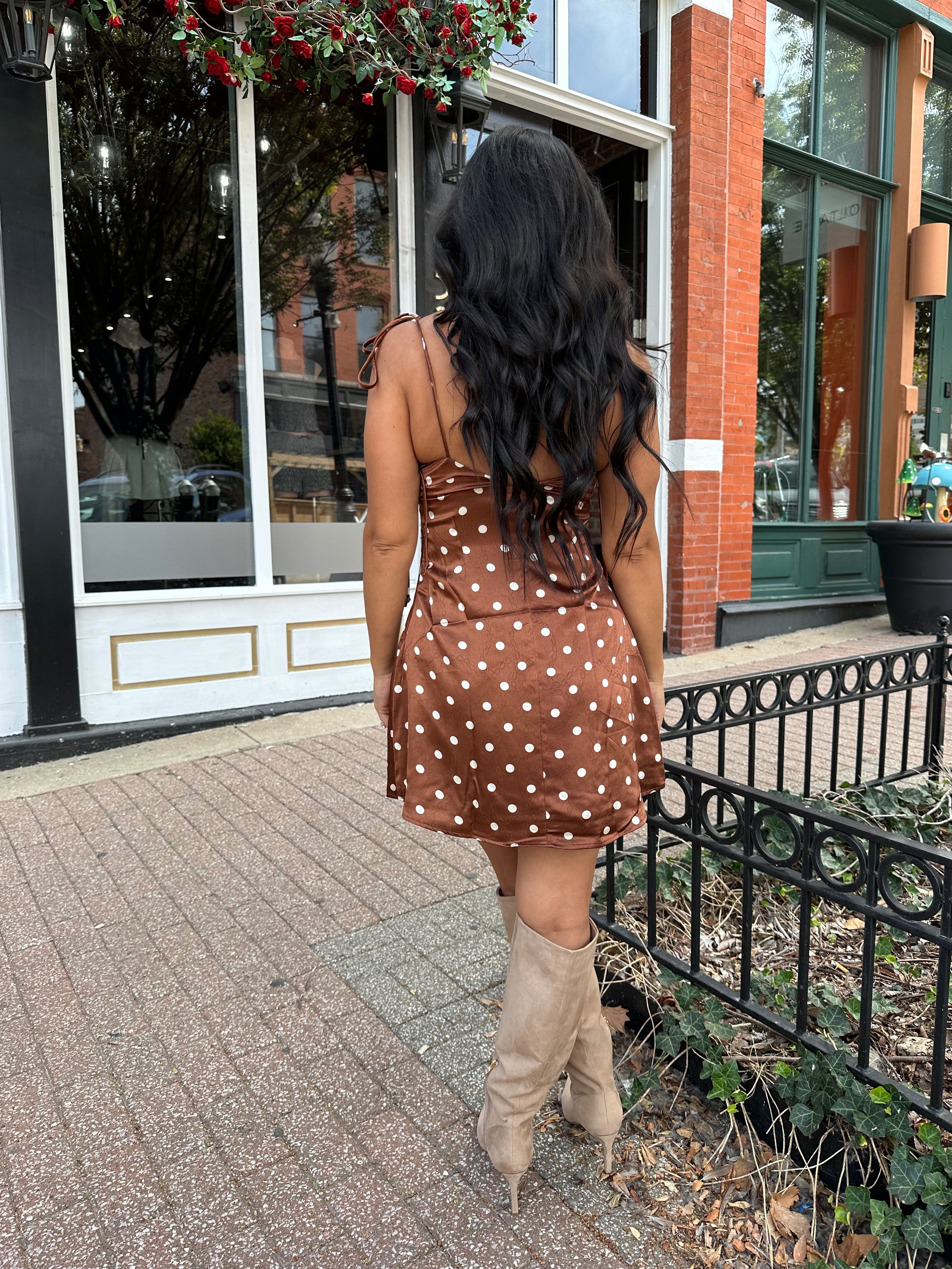 Woman wearing copper brown satin mini dress with white polka dots and self tie straps.