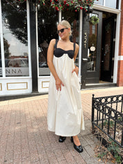 Woman wearing two tone maxi dress with black top and beige bottom with tie back. 
