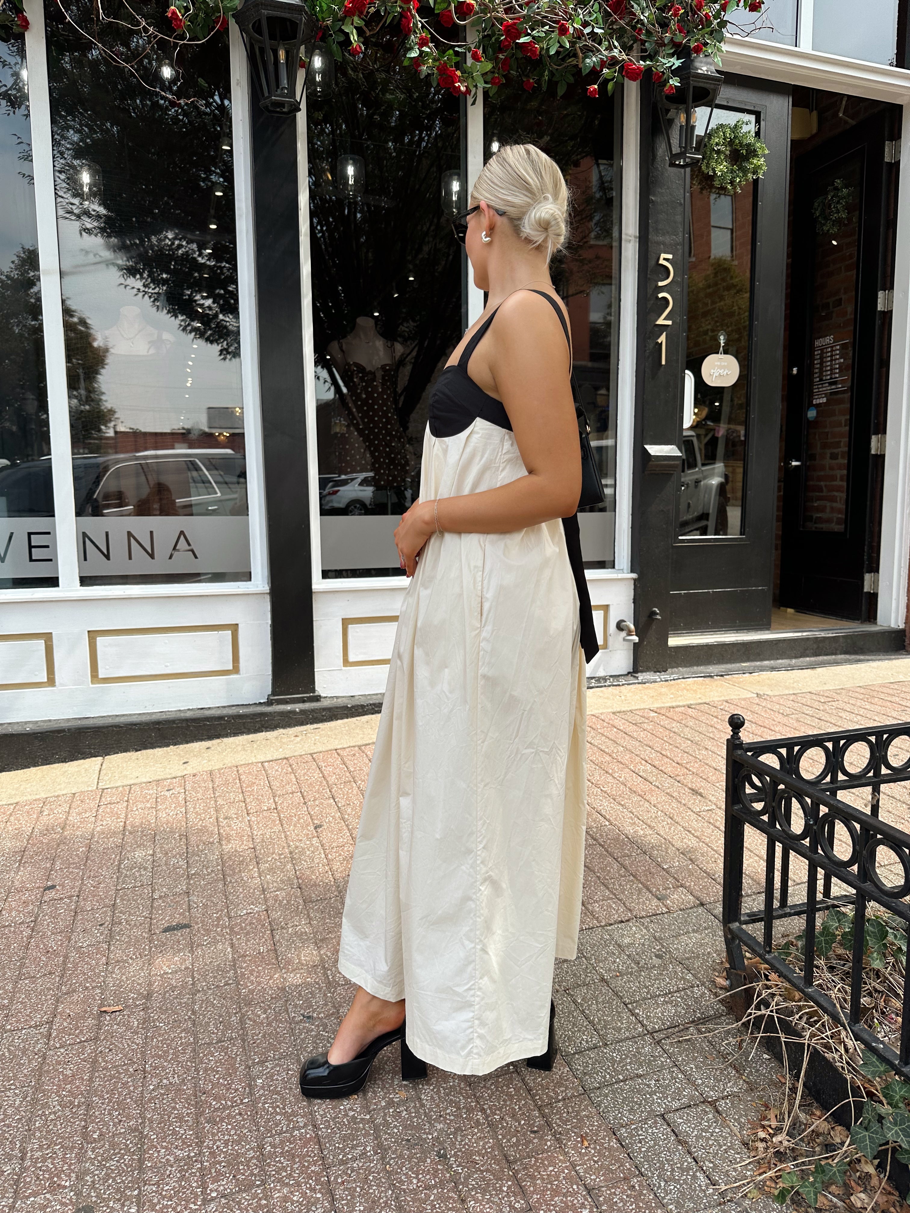 Woman wearing two tone maxi dress with black top and beige bottom with tie back. 