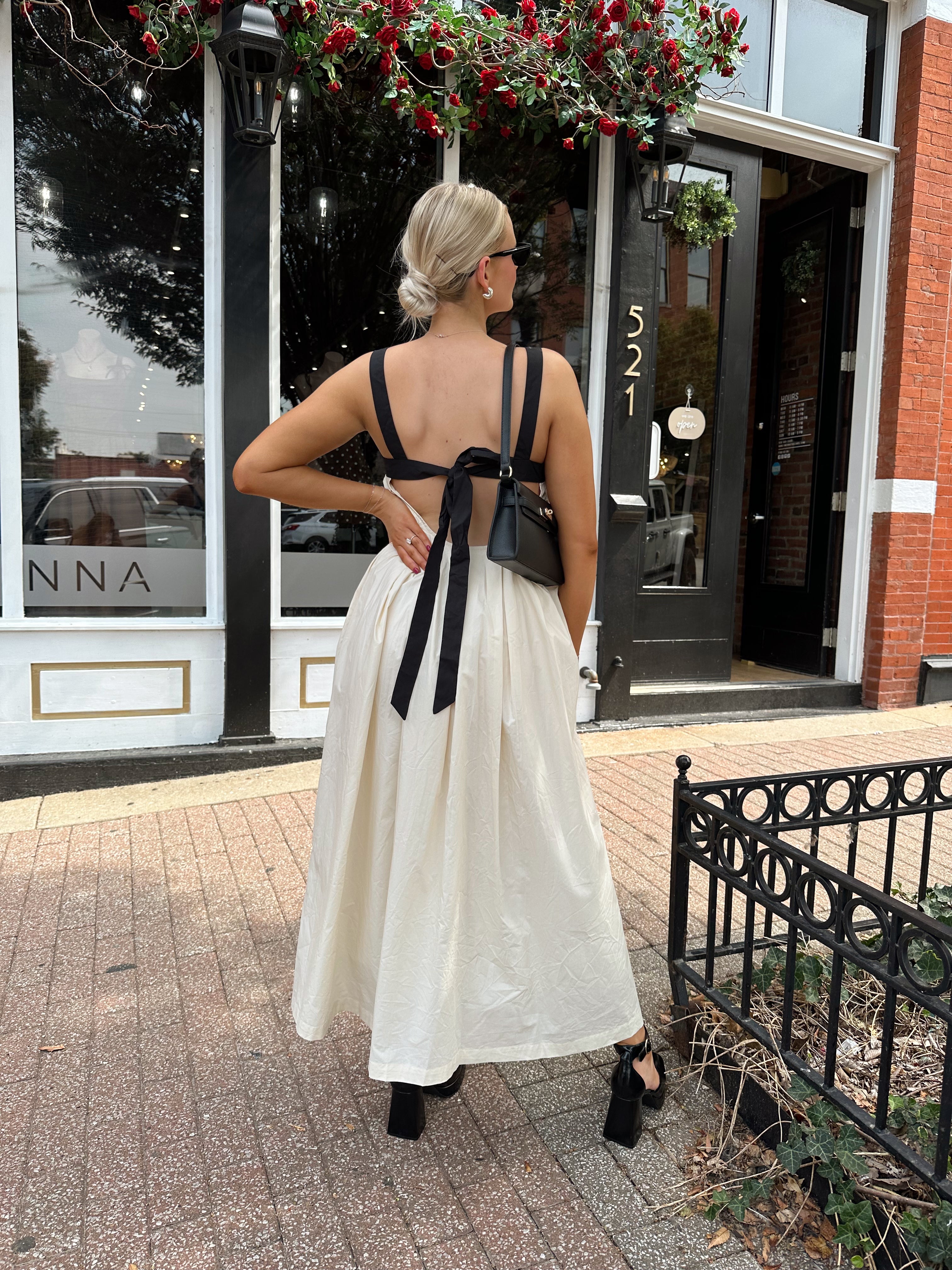 Woman wearing two tone maxi dress with black top and beige bottom with tie back. 