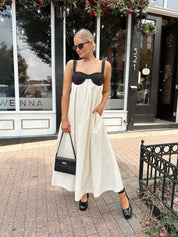 Woman wearing two tone maxi dress with black top and beige bottom with tie back. 