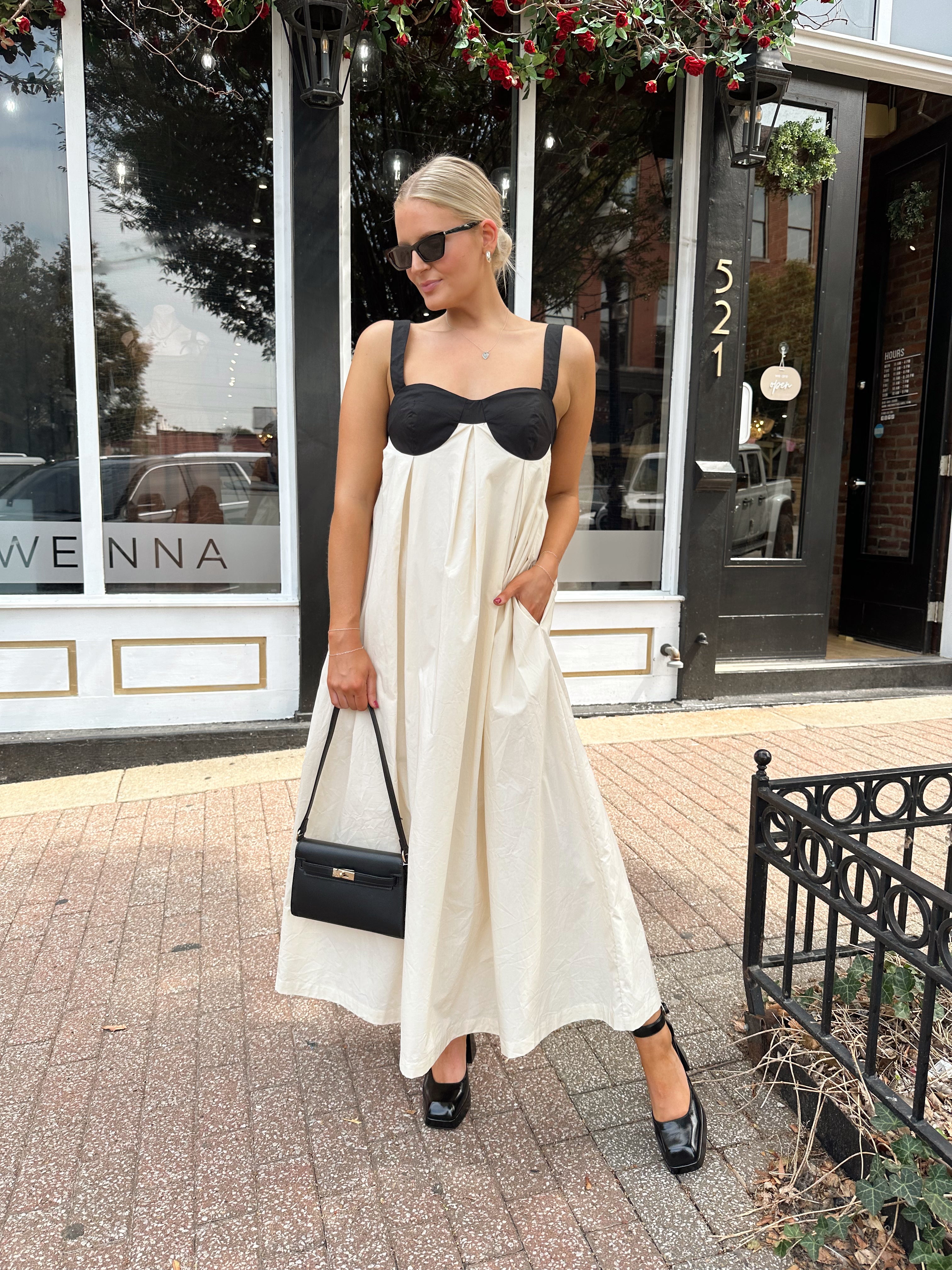 Woman wearing two tone maxi dress with black top and beige bottom with tie back. 