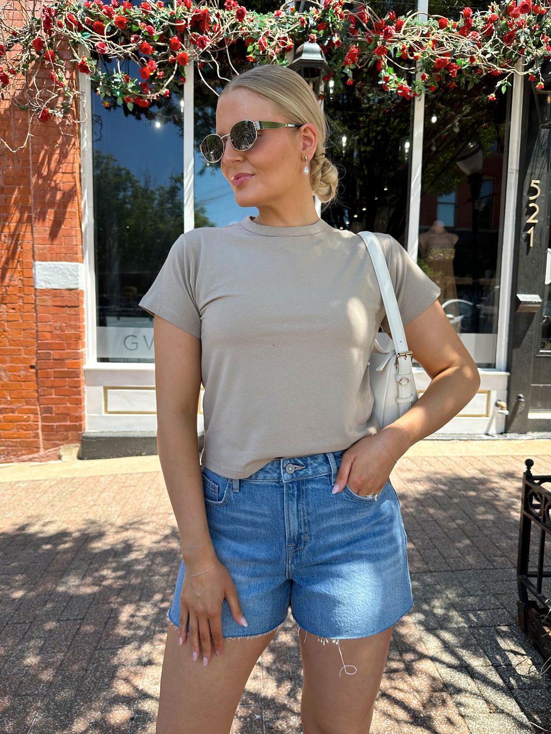 Woman wearing taupe baby tee with medium wash denim shorts. 